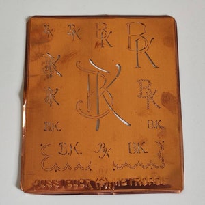 Peut inclure: Un pochoir en métal de couleur cuivre avec différents motifs des lettres "B.K." dans différents styles. Le pochoir est étiqueté "JUST-RITE" et "METROPOLE".