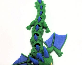 May include: A green and blue articulated dragon toy. The dragon has a segmented body, blue wings, and blue spikes along its back. The toy is designed to be flexible and poseable, with a detailed, textured surface.