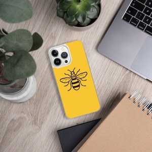 Puede incluir: Una funda de teléfono amarilla con un diseño de abeja negra. La abeja es el símbolo de Manchester, Inglaterra.