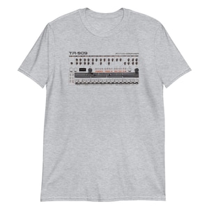 May include: A gray t-shirt with a vintage image of a Roland TR-909 Rhythm Composer drum machine. The machine has a black and white design with red buttons and a black display.