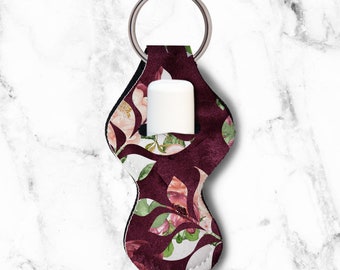 Könnte beinhalten: Ein Lippenbalsamhalter mit floralem Muster in Burgunderrot und Weiß mit einem silbernen Schlüsselring. Der Halter hat eine Tasche für eine Lippenbalsamtube.