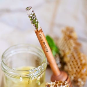 May include: A wooden honey dipper with a clear resin section containing pressed flowers. The dipper is engraved with the text "Garry 9-1-23".