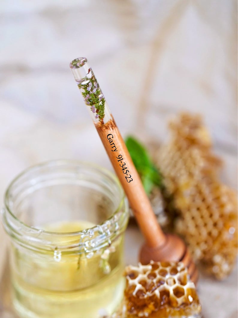 May include: A wooden honey dipper with a clear resin section containing pressed flowers. The dipper is engraved with the text "Garry 9-1-23".