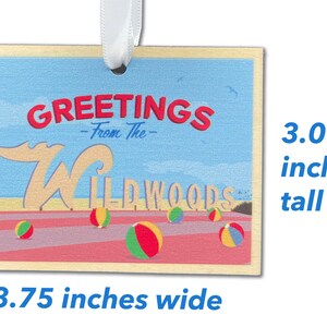 May include: A wooden ornament with a blue sky, beach, and the words "Greetings from the Wildwoods" in red and white. The ornament is 3.75 inches wide and 3 inches tall.
