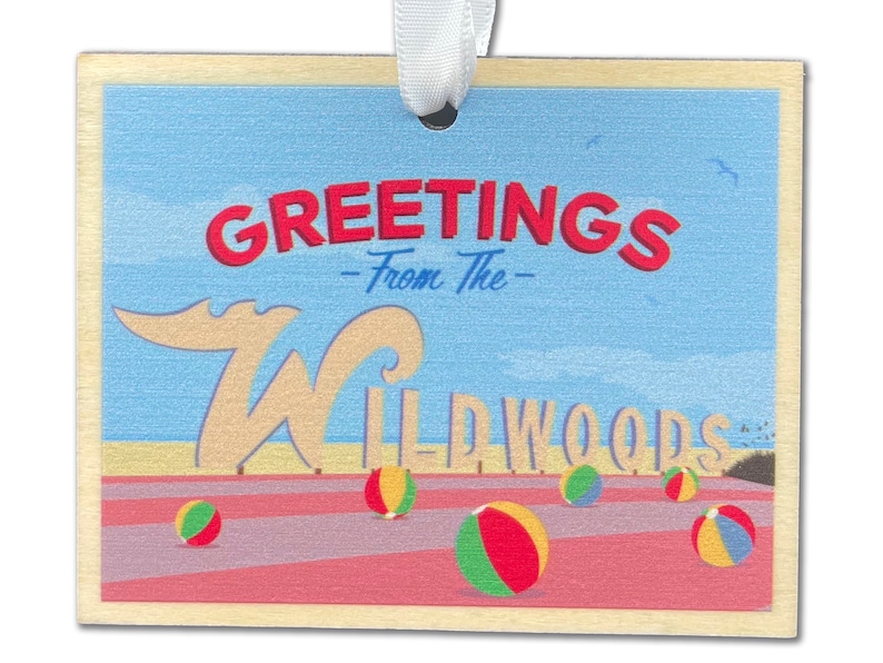 May include: A wooden postcard with a blue sky and beach scene. It says "Greetings - From The - Wildwoods" with a large white "W" and beach balls.