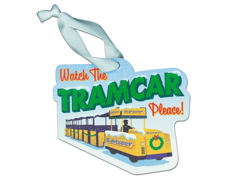 Puede incluir: Un adorno navide&ntilde;o amarillo y verde con forma de tranv&iacute;a con el texto "Watch the Tramcar Please!" en &eacute;l. El tranv&iacute;a est&aacute; decorado con una corona y la palabra "Sightseer" en el lateral.