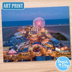 May include: Art print featuring a vibrant aerial view of a boardwalk at dusk. A large, illuminated Ferris wheel dominates the scene, surrounded by amusement park rides and buildings. The text "Beach Day Gifts.com" and "Beach Day Gifts & More" are visible.
