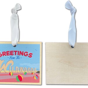 May include: A wooden ornament with a white ribbon. The front of the ornament has a blue sky background with the text "Greetings - From The - Wildwoods" and a red, white, and blue beach ball. The back of the ornament is plain wood.