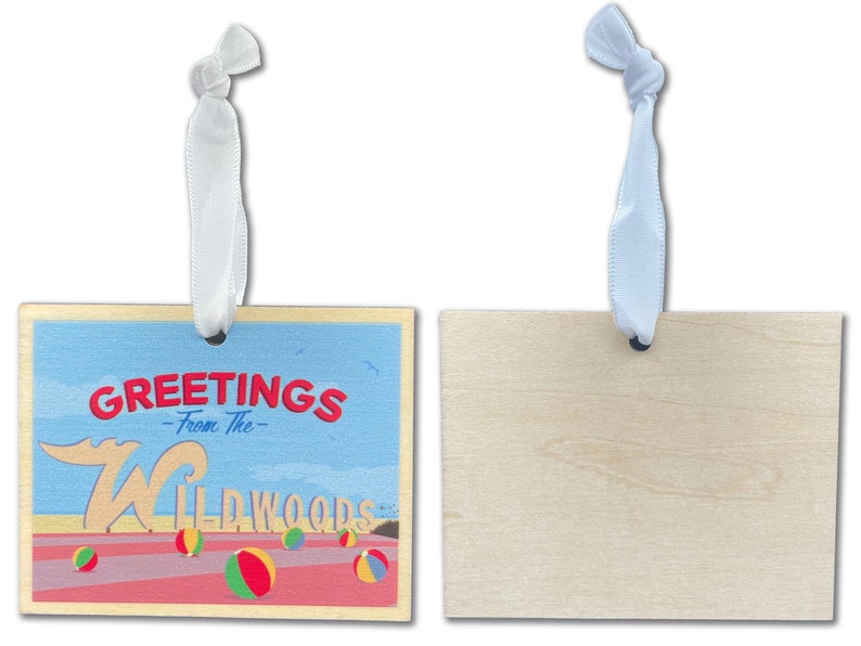 May include: A wooden ornament with a white ribbon. The front of the ornament has a blue sky background with the text "Greetings - From The - Wildwoods" and a red, white, and blue beach ball. The back of the ornament is plain wood.
