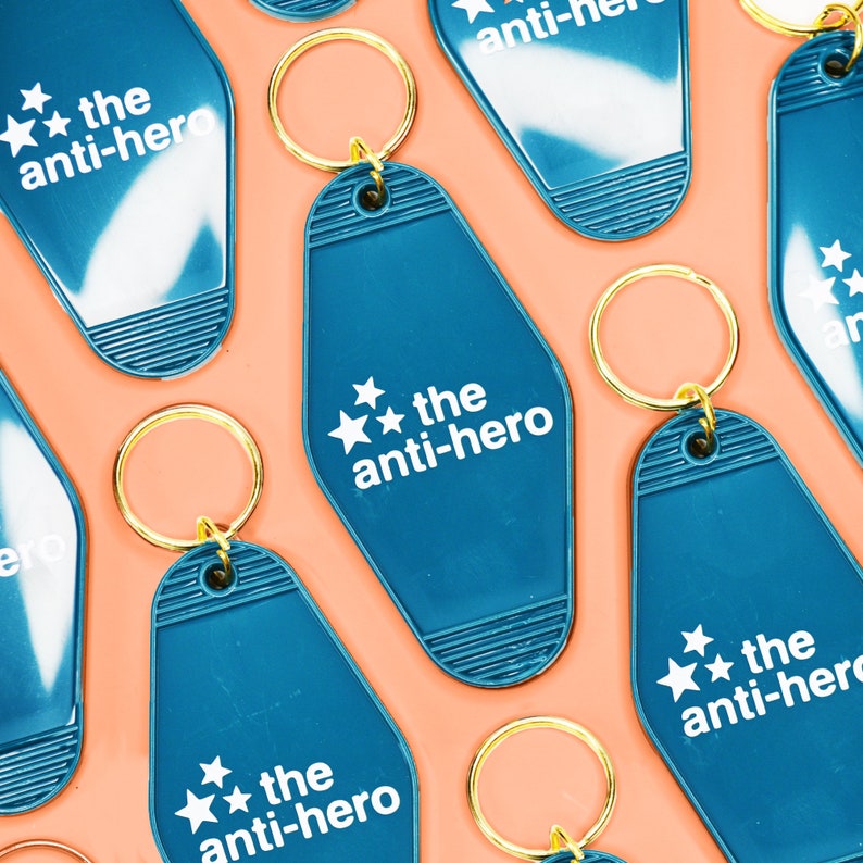 Pu&ograve; includere: Un set di portachiavi a forma di chiave di motel blu turchese con anelli dorati. Ogni portachiavi presenta stelle bianche e il testo "the anti-hero".