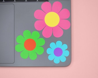 May include: A laptop computer with three colorful paper flowers attached to the lid. The flowers are pink, green, and blue with yellow, orange, and purple centers.