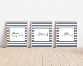 Peut inclure: Trois impressions d'art encadrées avec des dessins détaillés à la plume et à l'encre de poissons. Chaque impression a un fond blanc avec une illustration de poisson, dans un cadre à rayures bleues et blanches. Les cadres sont en bois clair, créant un thème nautique.