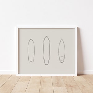 May include: A white framed print with a beige background featuring three black line drawings of surfboards.