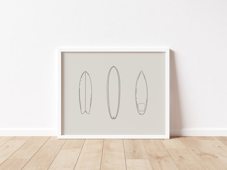May include: A white framed print with a beige background featuring three black line drawings of surfboards.