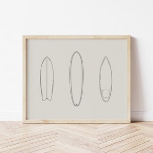 May include: A framed print with a minimalist line drawing of three surfboards on a beige background.