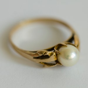 Puede incluir: Un anillo de oro con una perla engastada en una garra. El anillo es simple y elegante.