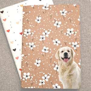 May include: Two notebooks. One has a tan floral pattern with a smiling golden retriever. The other has a white background with hearts in various colors. The notebooks are open, showing the inside pages.
