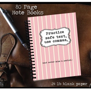 Può includere: Un quaderno a spirale con una copertina a righe rosa e bianche. La copertina presenta il testo "Practice safe text, use commas, (and never miss a period.)". Il quaderno è etichettato "80 Page Note Books" e "24 lb blank paper". Una penna poggia su una superficie in pelle.