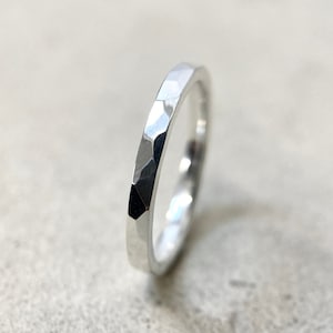 Peut inclure: Une bague en argent avec un design à facettes. La bague présente un motif géométrique avec de multiples surfaces planes qui réfléchissent la lumière. C'est une simple alliance, adaptée au quotidien.