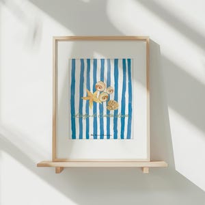 Peut inclure: Impression d'art encadrée avec un fond à rayures bleues et blanches, ornée d'illustrations de coquillages et d'une étoile de mer. L'œuvre est présentée sur une étagère en bois clair, dans un cadre en bois naturel.