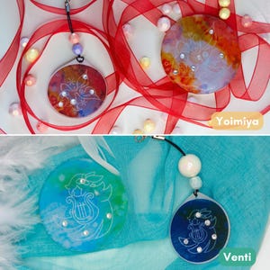 May include: Two circular Yoimiya charms featuring red, orange, and yellow ink patterns with white line art and rhinestones, and two circular Venti charms in blue and green ink patterns with white line art, rhinestones, and white beads on black cords.