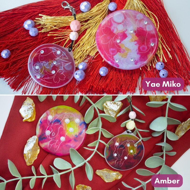May include: Two circular resin charms featuring Yae Miko and Amber designs. The Yae Miko charm is pink with white line art and rhinestones, while the Amber charm is multicolored with white line art and rhinestones. Both include small beads.