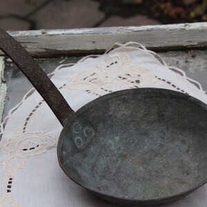 Peut inclure: Une louche en cuivre vintage avec une longue poignée en fer rouillée. La louche est posée sur une dentelle blanche.