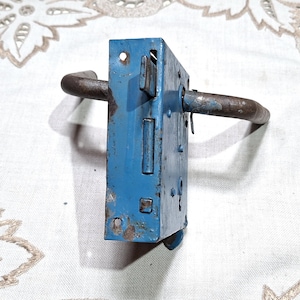 May include: A vintage blue metal door lock with a curved handle. The lock has visible signs of wear and rust, suggesting age. The handle is a dark, weathered metal. The lock is rectangular and has several holes and mechanisms visible.