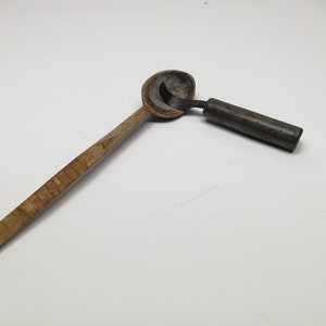 May include: A vintage wooden scoop with a long handle and a metal attachment. The scoop is made of light-colored wood with a dark metal piece attached to the bowl. The handle is rectangular and the metal piece has holes.