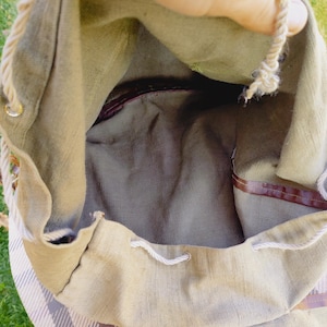 Op de afbeelding: Een beige canvas trekkoordtas met een bruine leren bies en een wit touw trekkoord. De tas is open en de binnenkant is zichtbaar.