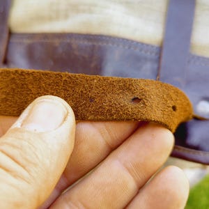 Op de afbeelding: Close-up van een bruine leren riem met twee gaten. De riem is bevestigd aan een groter stuk leer.