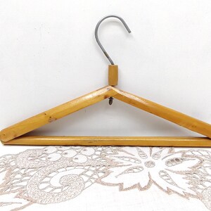 May include: A wooden hanger with a metal hook. The hanger is made of light brown wood and has a simple design.