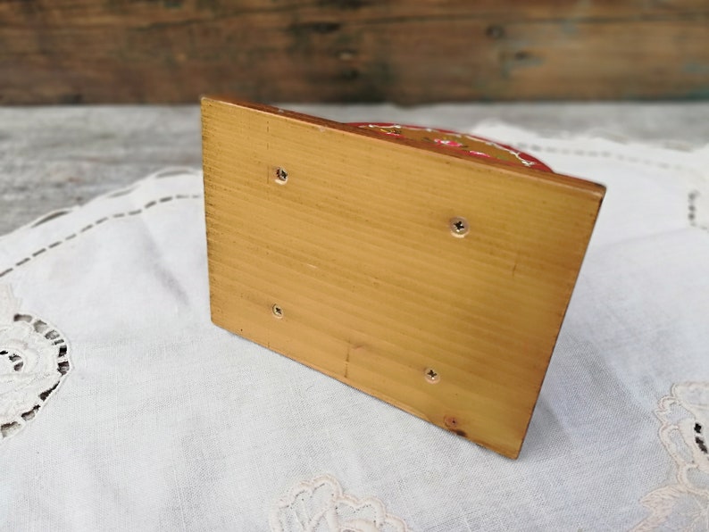 May include: The bottom of a wooden napkin holder with a light brown finish. The holder has four small screws on the bottom.
