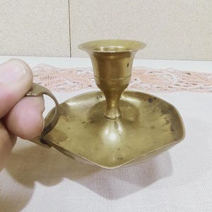 Puede incluir: Un candelero de latón con un diseño sencillo. El candelero tiene una base redonda y una sola copa para la vela.