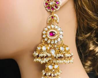May include: Gold earrings with pink and white stones, featuring a floral design and three dangling bells.