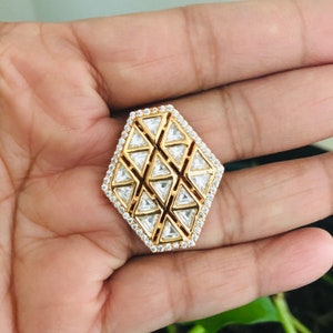 May include: A gold ring with a geometric design featuring a pattern of small, clear cubic zirconia stones.