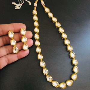 May include: A gold necklace and earrings set with teardrop-shaped white stones. The necklace is made of a gold chain with a series of teardrop-shaped stones.