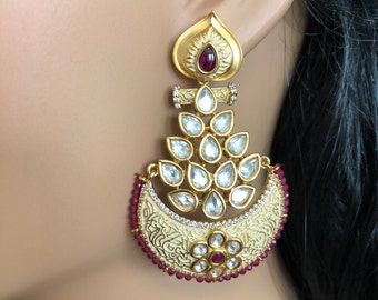 May include: Gold tone earrings with a crescent moon design, white stones, and pink beads. The earrings have a teardrop-shaped top with a pink stone.