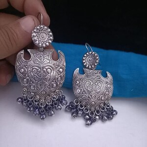 May include: A pair of silver earrings with intricate floral designs and dangling beads. The earrings are shaped like a heart with a decorative border.