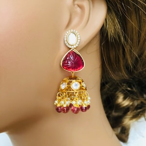 May include: Gold earrings with a pink teardrop-shaped stone, a round white stone, and a dangling cluster of pink and white beads.