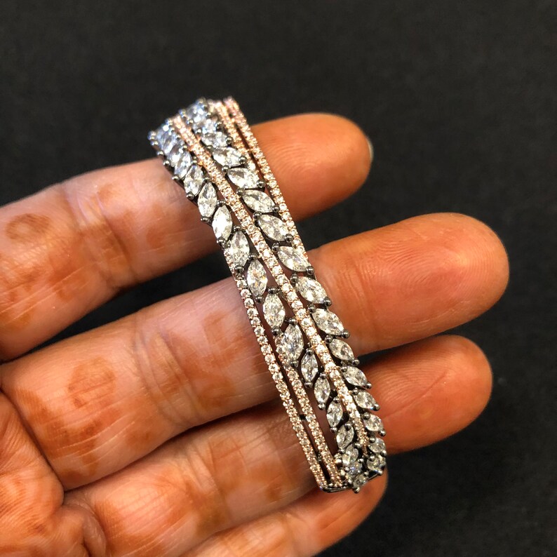 Puede incluir: Un brazalete de plata y oro rosa con una fila de piedras transparentes en forma de marquesa.
