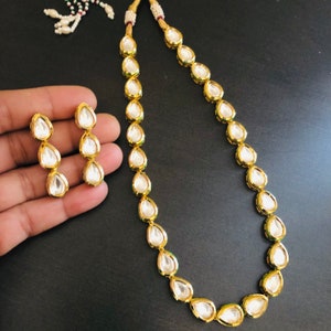 May include: A gold necklace with a teardrop-shaped pendant and matching earrings. The necklace is made of small, round beads and the pendant is set with a clear stone. The earrings are also set with clear stones.