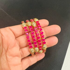 May include: Four gold bangles with pink stones and clear rhinestones. The bangles are stacked on top of each other.