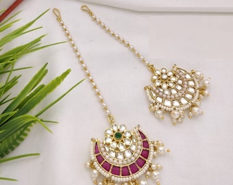 May include: A pair of gold-tone maang tikka headpieces with pearl and mirror embellishments. One maang tikka features a pink and green stone design, while the other has a green stone design.