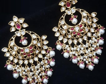 May include: A pair of gold earrings with intricate designs, featuring white pearls, red gemstones, and a dangling chain of pearls.