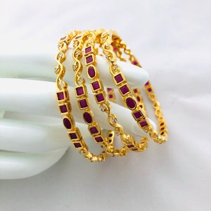 Puede incluir: Conjunto de cuatro brazaletes de oro con piedras moradas y blancas. Los brazaletes están decorados con un diseño de espiral y piedras cuadradas y ovaladas.