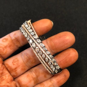 Puede incluir: Un brazalete de plata y oro rosa con una fila de piedras transparentes en forma de marquesa.
