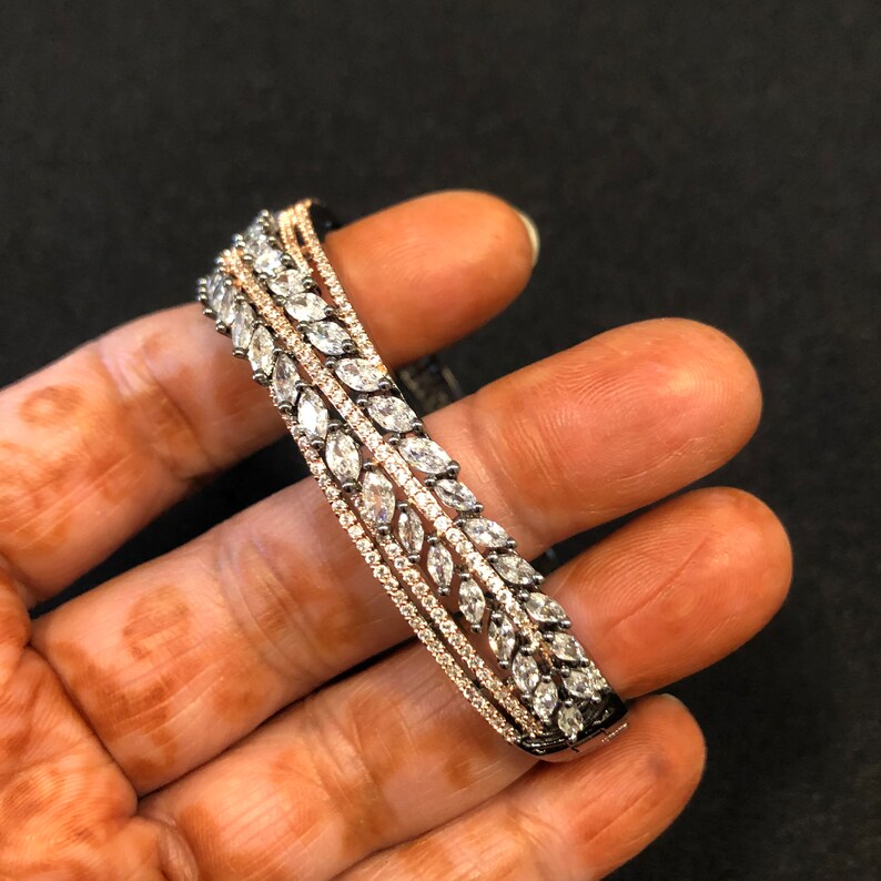 Puede incluir: Un brazalete de plata y oro rosa con una fila de piedras transparentes en forma de marquesa.