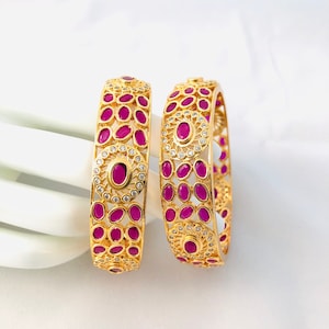 May include: Two gold bangles with pink oval stones and white round stones set in a circular design.