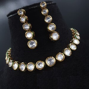 May include: A gold necklace and earrings set with a row of clear round stones with green accents.